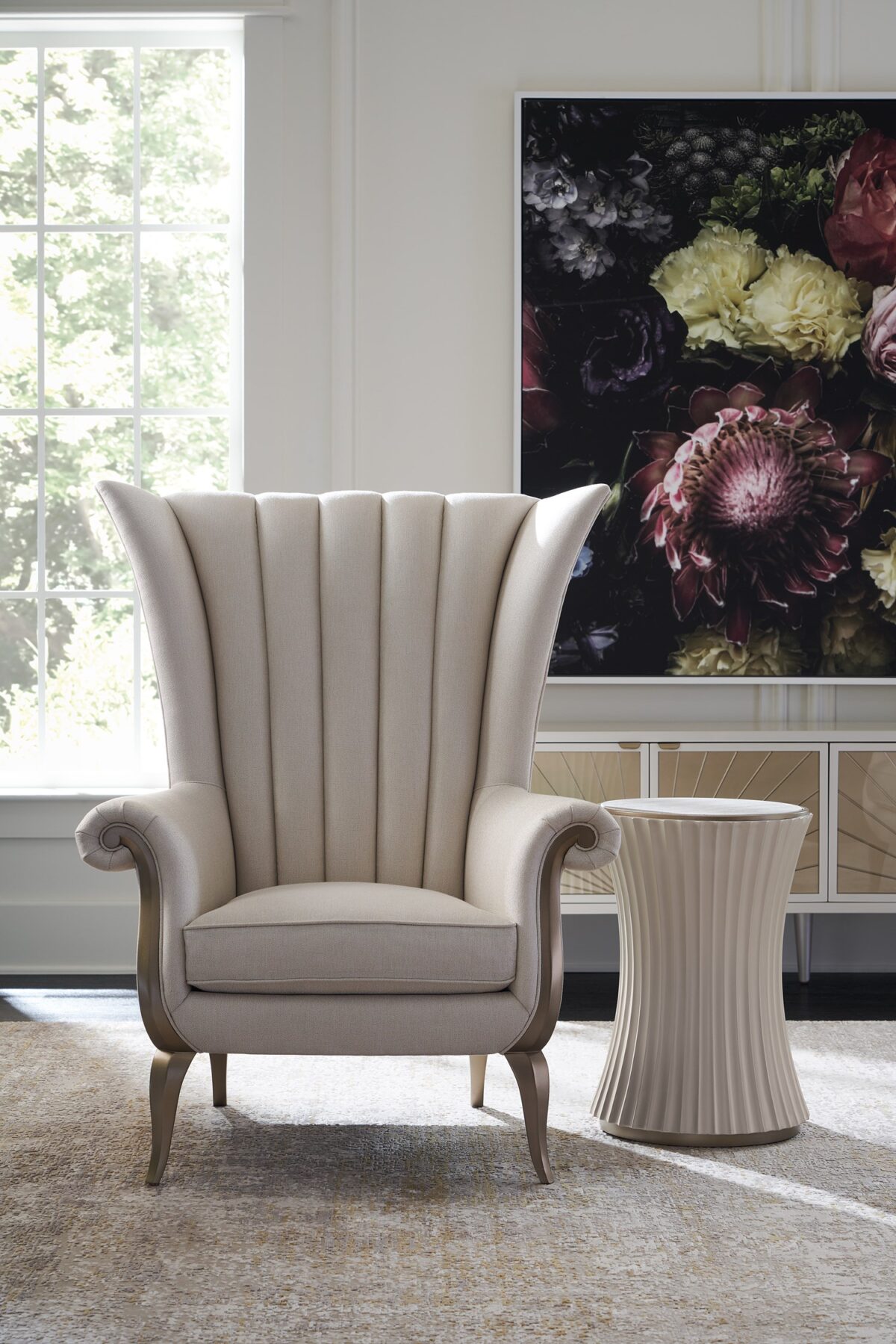 The Caracole Valentina Accent Chair, a sophisticated wing chair with a tall channel-tufted back, wood-trimmed roll arms, upholstered in a light cream pin-dot fabric, and featuring exposed wood details in a Golden Shimmer finish.