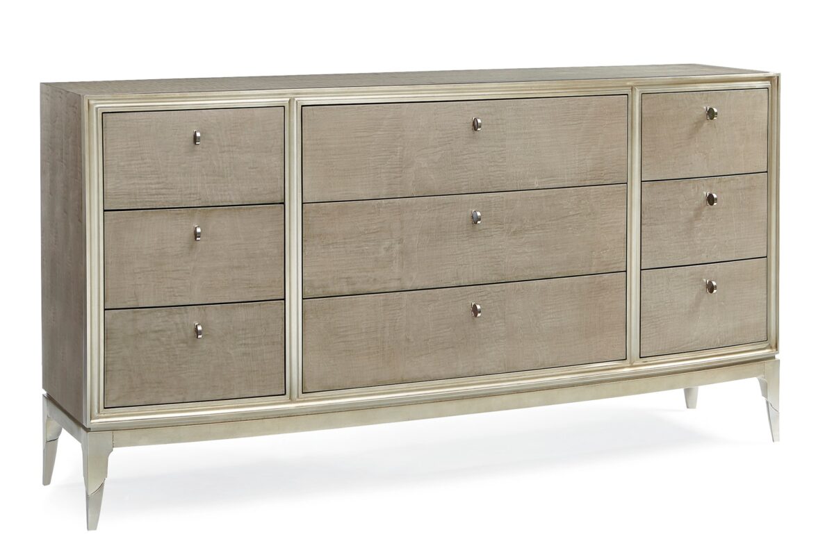 Made To Shine Dresser by Caracole — a 72″ wide nine-drawer dresser in Moonlit Sand–finished curly maple, accented with Soft Silver Leaf trim on the frame and base, topped by lightly brushed chrome metal ferrules on tapered legs, featuring antique silver knobs with black mother-of-pearl centers and soft-close undermount drawer guides.