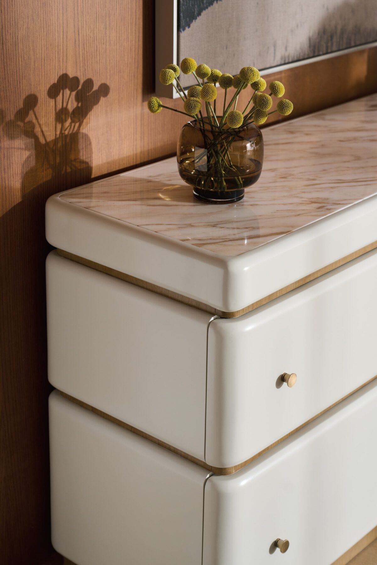 Milos Dresser by Caracole — a 65″‑wide modern dresser in Almond Milk finish with gently rounded stacked silhouette, featuring four soft‑close drawers trimmed in Toasted Pecan, topped with Calacatta Oro marble, and equipped with a removable felt‑lined tray in the top drawer.