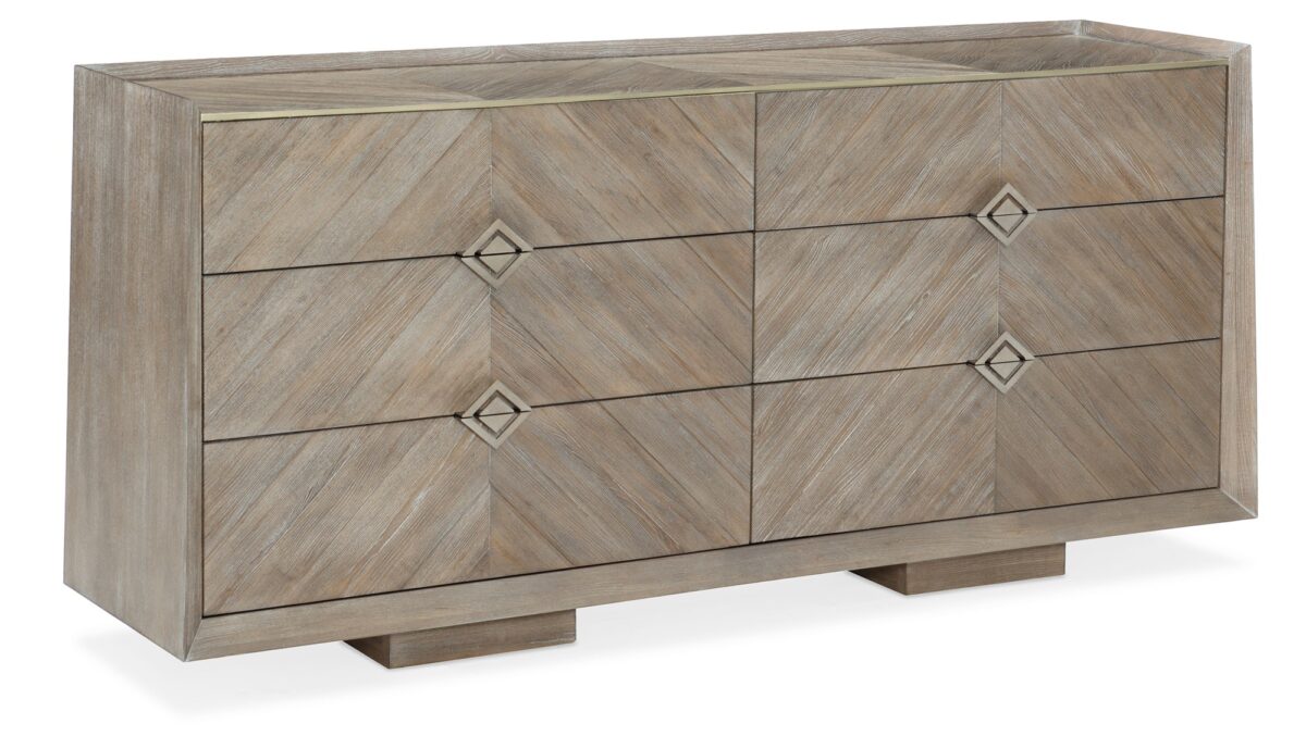 Naturally Dresser by Caracole — a 74″‑wide six‑drawer dresser in Ash Driftwood finish with chevron‑patterned wood‑veneer fronts, accented by a slender Sundance Gold metal bead edging and recessed drawer pulls, all sitting on low block feet.