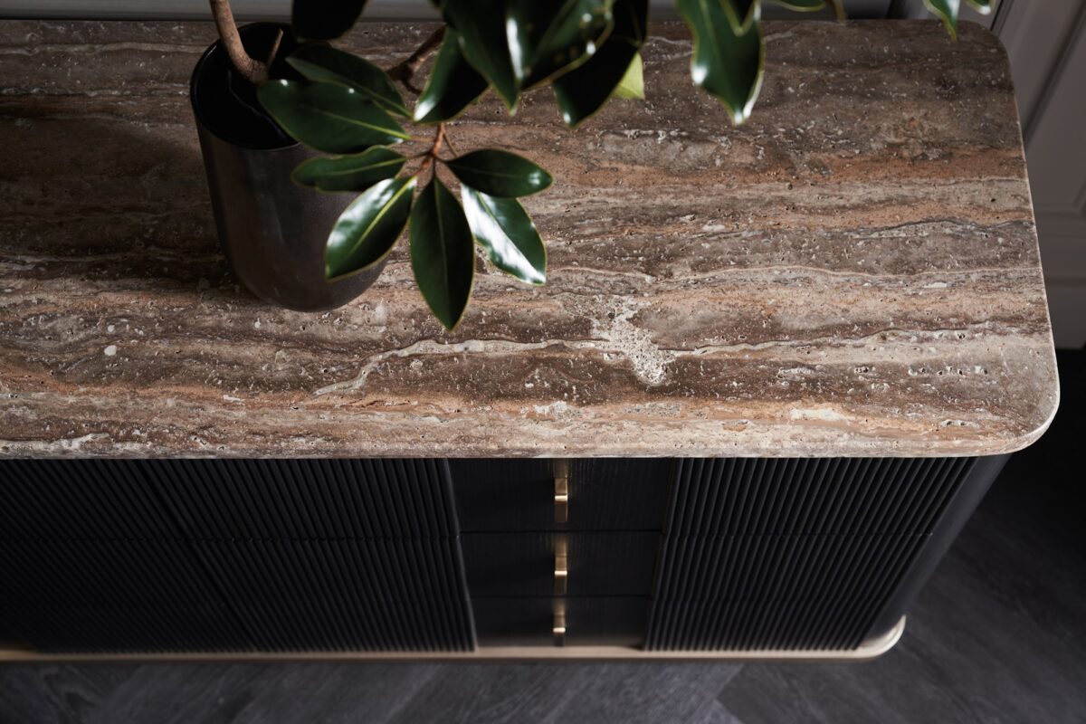Rhythm Dresser by Caracole — a 69½″ wide six-drawer dresser featuring tactile reeded drawer fronts in Sun Drenched Oak finish, topped with creamy Travertine stone and set on a low neutral‑metal plinth, with rounded corners, bronze bar pulls, and soft‑close undermount guides.