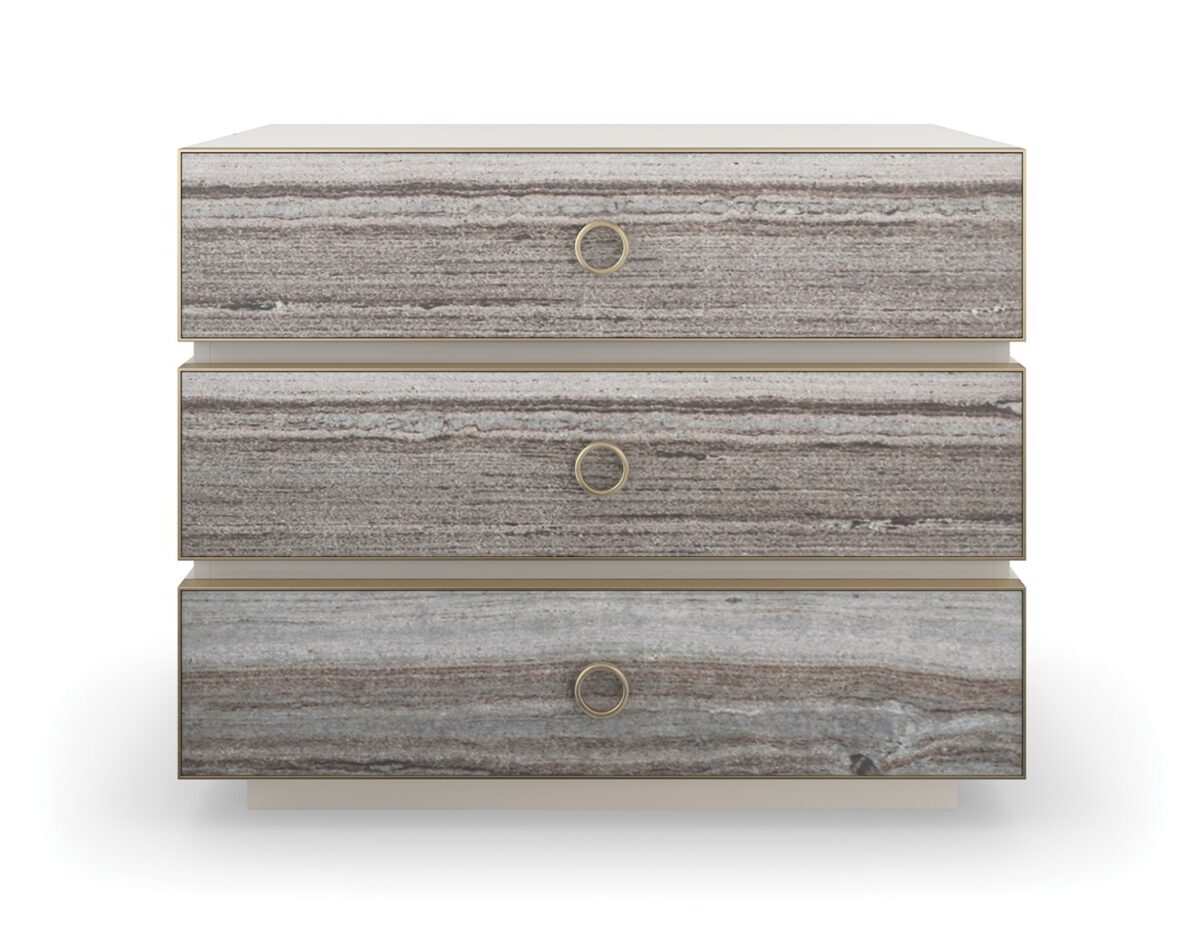 Bedrock Nightstand by Caracole — a 34″‑wide three‑drawer nightstand with polished gray sandstone fronts featuring subtle champagne‑gold trim and ring pulls, set in a creamy Almond Milk wood frame with a matching plinth base and soft‑close undermount drawer guides.