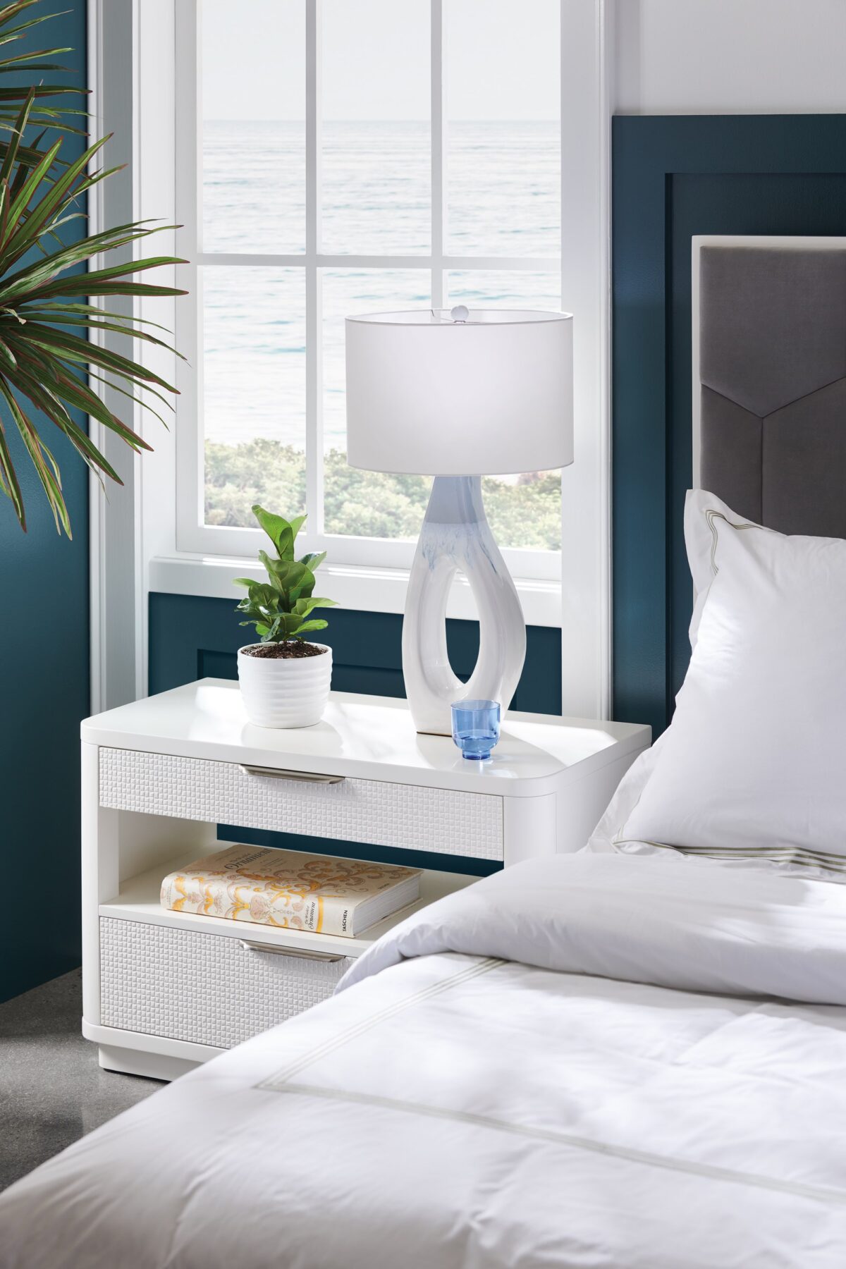 In Touch by Caracole" refers to a bedside table/nightstand. It's characterized by rounded edges, a clean-lined "Cloud White" finish, carved drawer fronts with a "woven mini-tile motif," finger-cup pulls in Satin Nickel, two drawers, and open center storage with a built-in light, a USB port, and wire management holes.