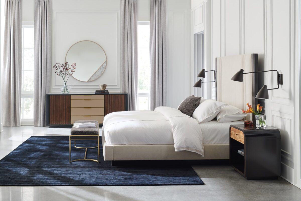 Caracole Decent Proposal King Bed featuring a light-toned performance fabric upholstered headboard, footboard, and side rails, with Dark Chocolate trim and Champagne Gold metal inlay accents, set on a Dark Chocolate plinth base.