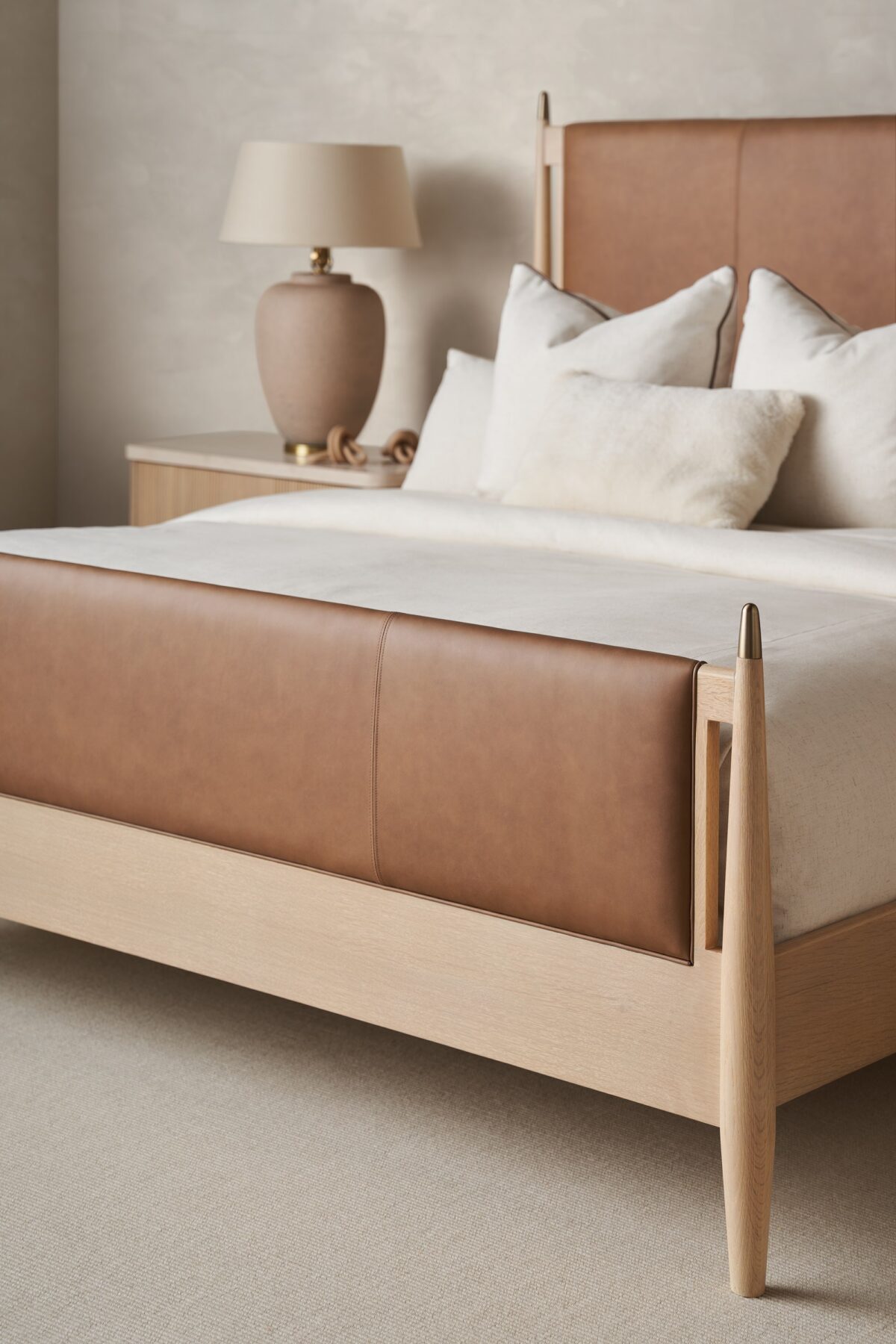 Caracole Rhythm King Bed featuring a luxurious camel-colored leather upholstered headboard and footboard, complemented by a Sun Drenched Oak wood frame with metal finials in Lucent Bronze finish, designed with clean, parsons-style lines.