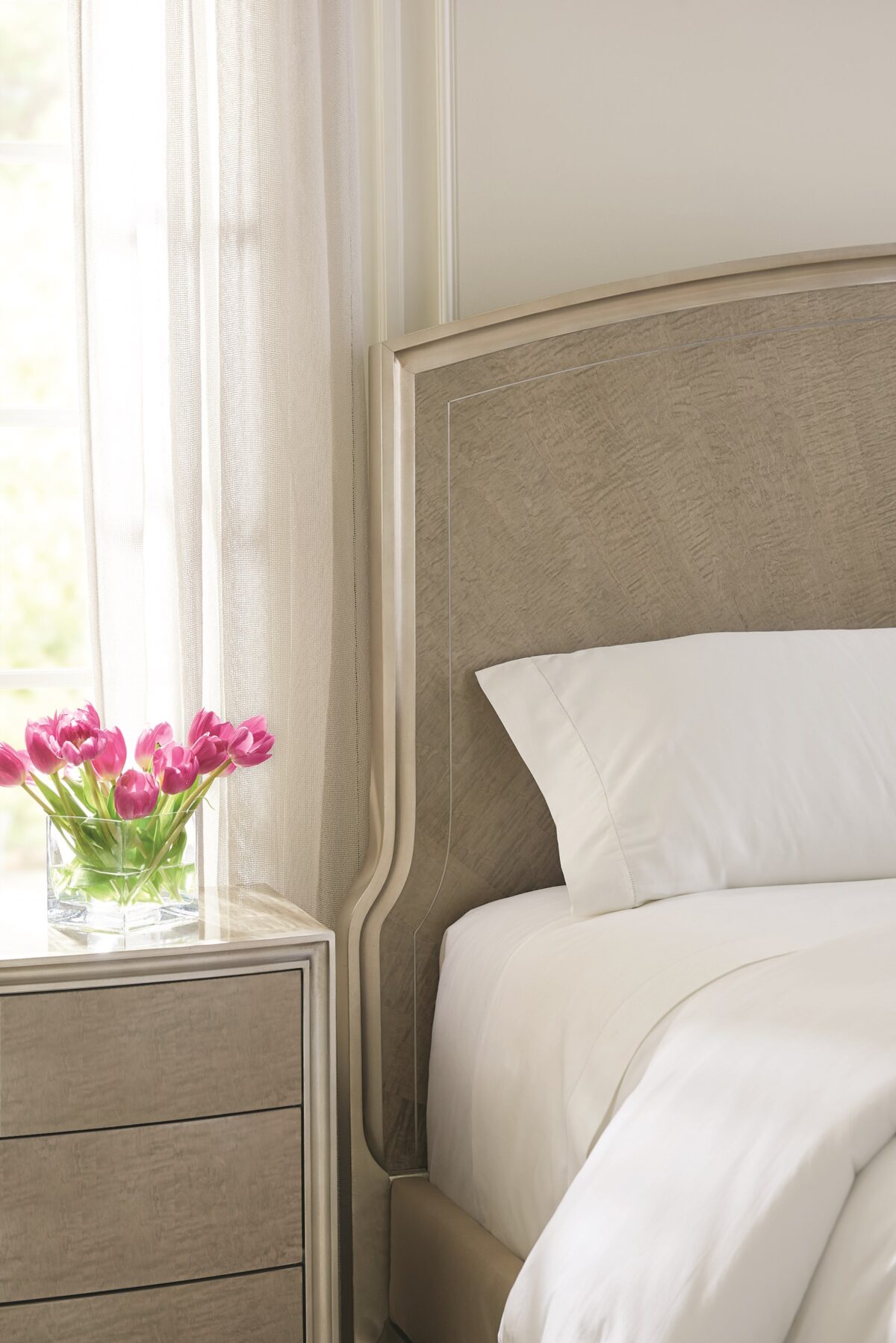 Caracole Rise To The Occasion King Bed featuring a gracefully curved headboard outlined with a metal inlay, crafted from Silver Curly Maple veneers in a Soft Silver Leaf finish, complemented by a Moonlit Sand frame and Lightly Brushed Chrome metal ferrules on the legs.