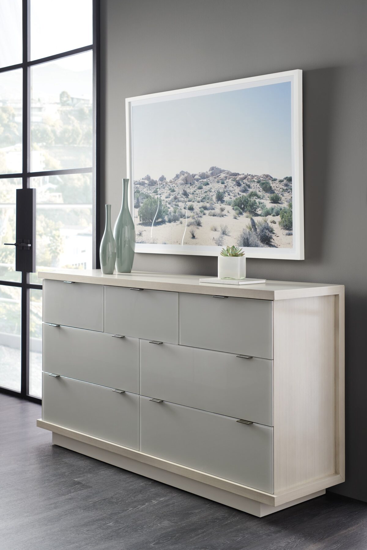 Expressions Dresser by Caracole — a 66″‑wide contemporary dresser with seven back‑painted glass drawer fronts in delicate gray, set within an ash‑taupe hardwood case, featuring notched-tab pulls, soft‑close undermount guides, a low plinth base, and USB ports integrated on both sides.