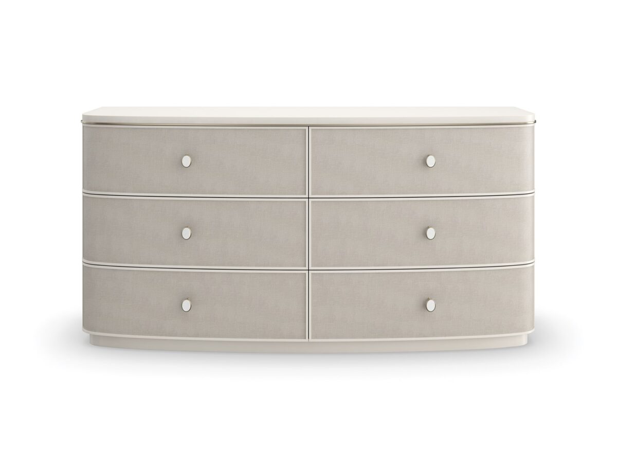 Lyon Dresser by Caracole — a 64″‑wide sculptural dresser in Almond Milk faux‑linen vinyl finish, with softly curved sloping sides and six vinyl‑wrapped drawers featuring painted Interiors, all set on a clean plinth base and trimmed with a slender Brushed‑Gold metal bead.