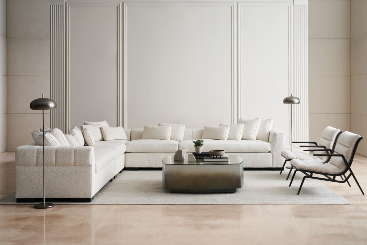Caracole Fret Knot Corner featuring a carved fret panel inspired by a narrow castle window, Soft Silver Paint finish, fluted conical legs, and a supportive eight-way hand-tied seat.