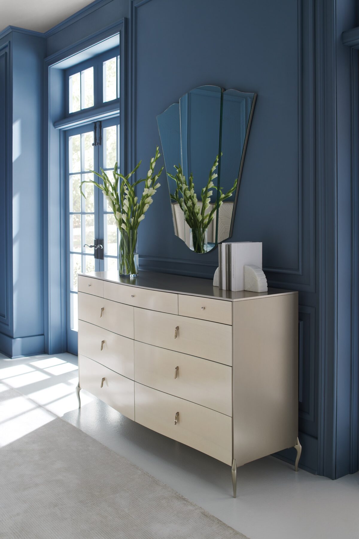 Dress to Impress Dresser by Caracole — a 62″ wide nine‑drawer dresser in soft‑silver painted Asian hardwood case, with vanilla‑cream figured‑sycamore drawer fronts, elongated Art‑Deco style metal pulls, a gently curved top, ornate silver‑toned legs, and two felt‑lined top drawers.