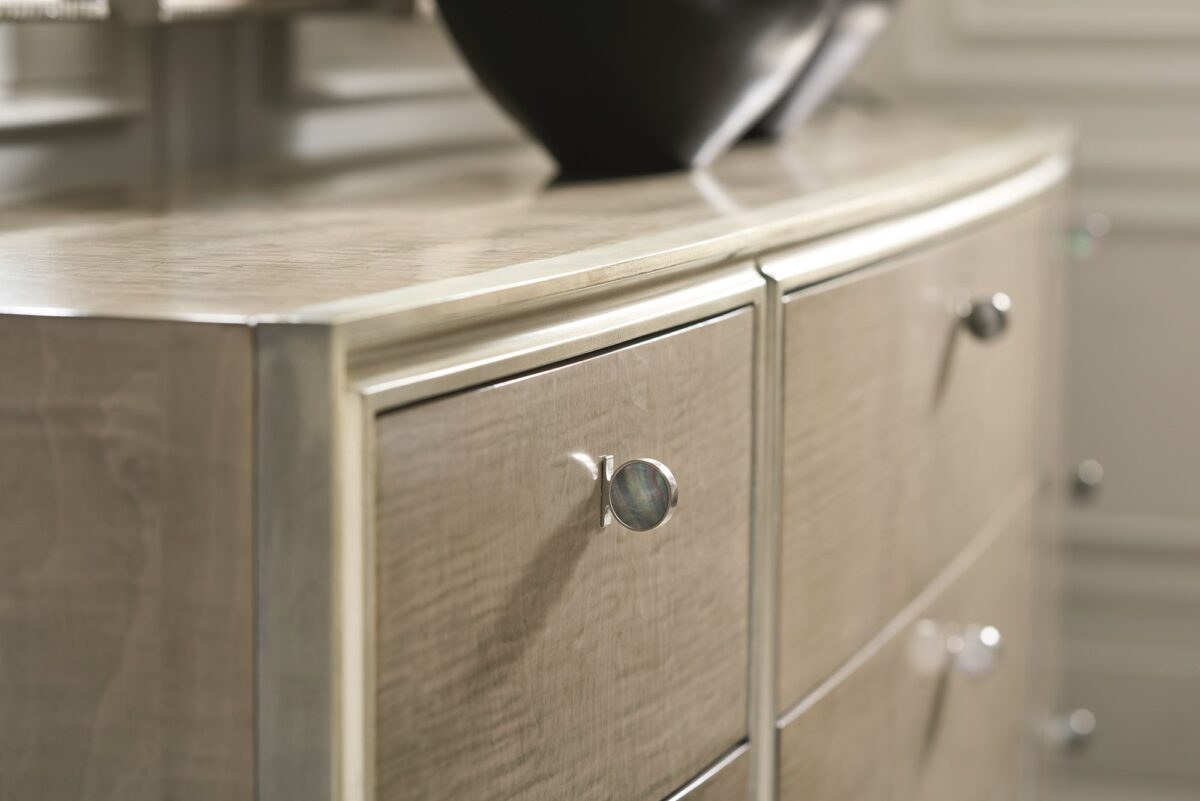 Made To Shine Dresser by Caracole — a 72″ wide nine-drawer dresser in Moonlit Sand–finished curly maple, accented with Soft Silver Leaf trim on the frame and base, topped by lightly brushed chrome metal ferrules on tapered legs, featuring antique silver knobs with black mother-of-pearl centers and soft-close undermount drawer guides.