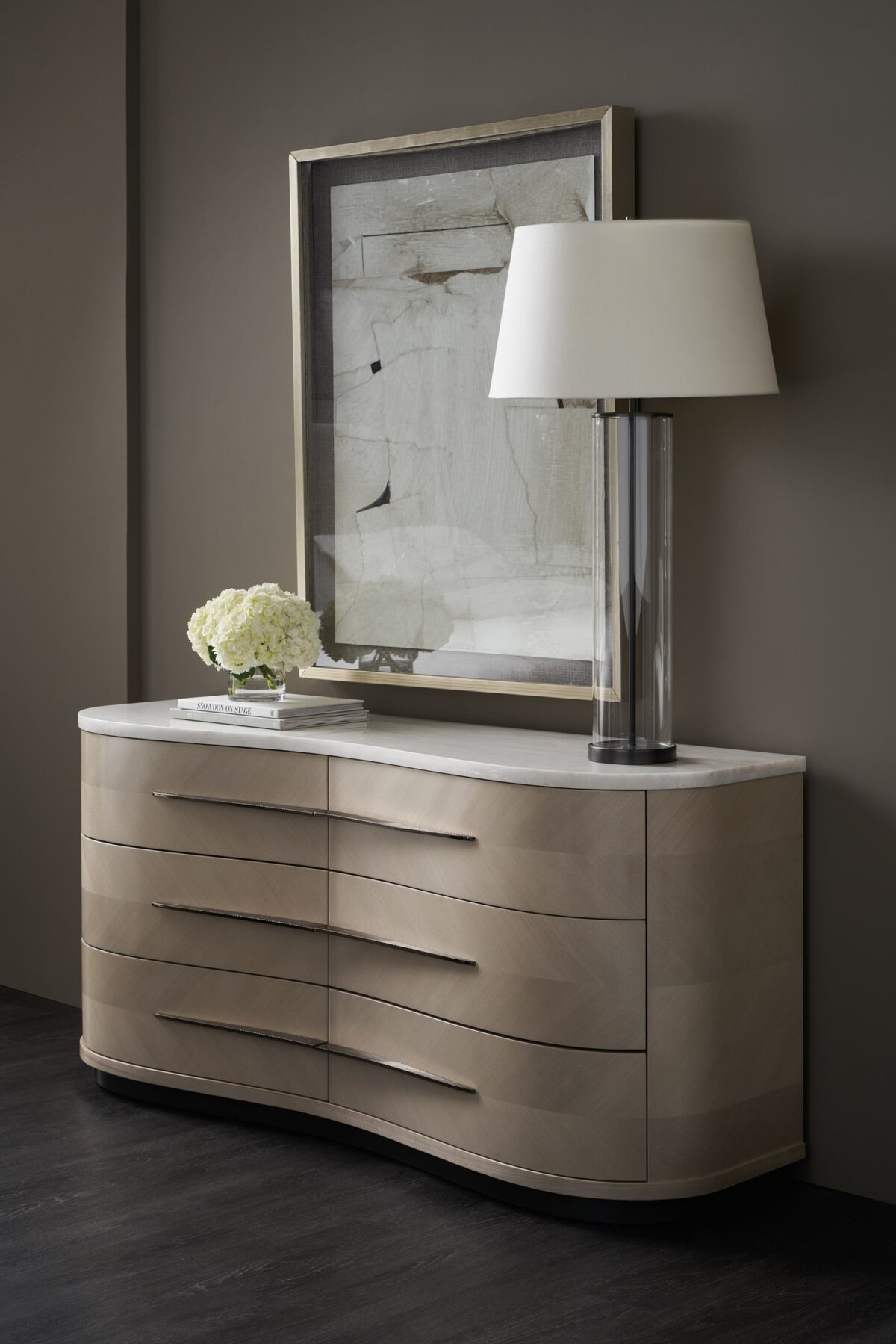 Roam Dresser by Caracole — a sleek 68″‑wide dresser in pearlescent Moonstone finish with six gently curved soft‑close drawers featuring horizontal Deep Bronze handles; chevron‑patterned Koto veneers flow organically across the fronts and end panels, topped with luxurious white Rhino marble and set atop a Seal‑Skin tone plinth base.