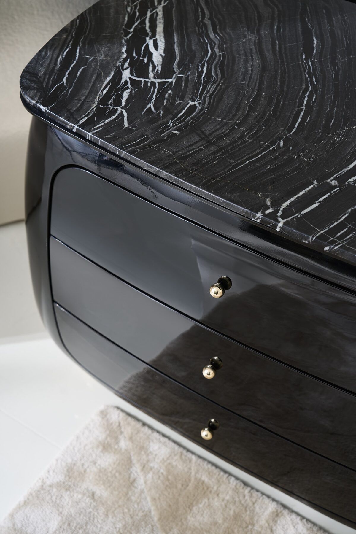 Cabochon Nightstand by Caracole — a 34″‑wide sculptural nightstand with a rounded Piano Black resin frame, featuring a flat Tree Black stone top with natural black and grey veining; three curved drawers with soft-close undermount guides and Piano Black interiors; Whisper of Gold spherical metal knobs and matching ball feet complete the luxurious design.