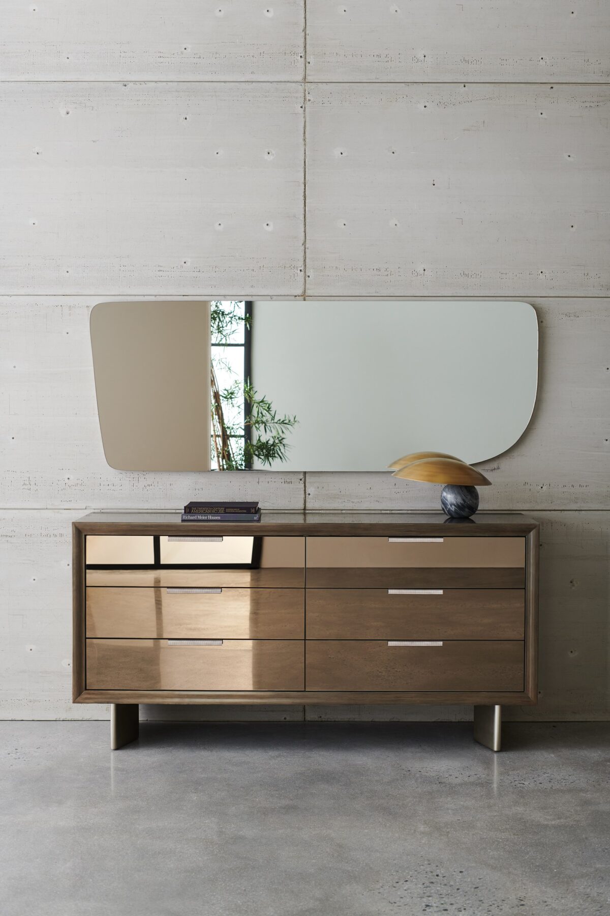 Fashion Dresser by Caracole — a curving six-drawer dresser in lustrous gold-leaf finish, topped with a mirrored bronze surface and slender tapered legs; each drawer features jewelry-like ring pulls and undermount soft-close operation.