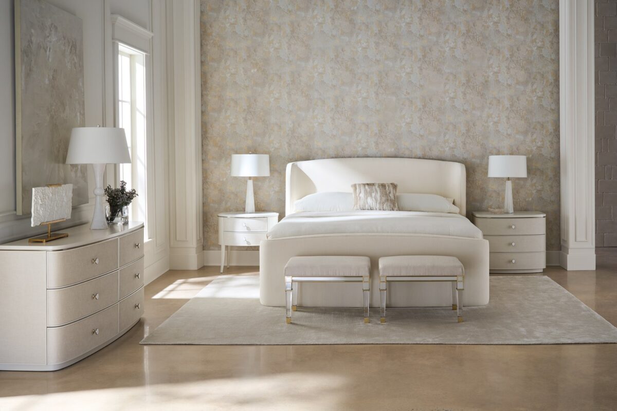 Lyon Dresser by Caracole — a 64″‑wide sculptural dresser in Almond Milk faux‑linen vinyl finish, with softly curved sloping sides and six vinyl‑wrapped drawers featuring painted Interiors, all set on a clean plinth base and trimmed with a slender Brushed‑Gold metal bead.