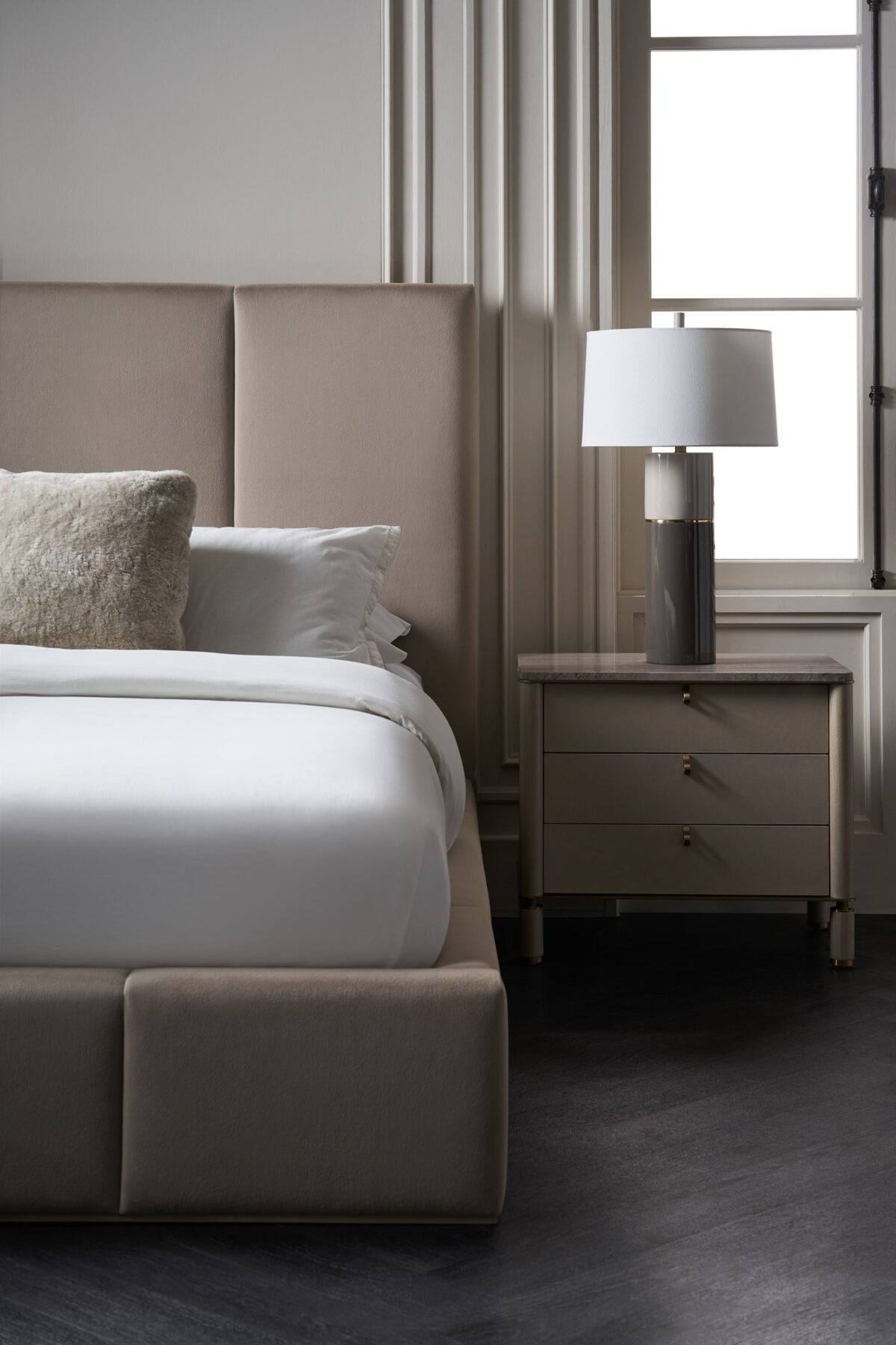 Balance Drawer Nightstand by Caracole — a 28″‑wide modern nightstand in Cremini-finished hardwood with three soft‑touch vinyl-wrapped drawers, topped in polished Silver Travertine stone and supported on round Cremini legs with Lucent Bronze-metal accents and trim.