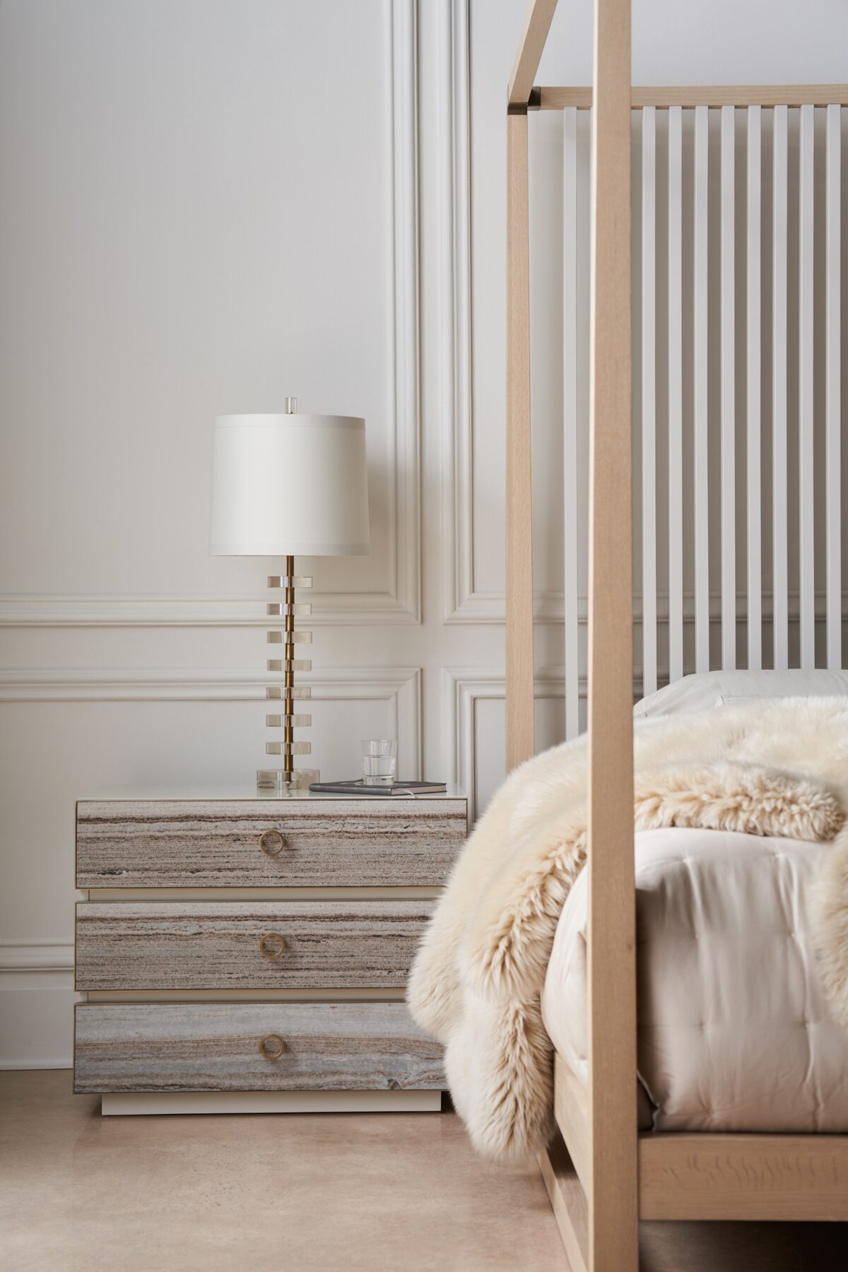 Bedrock Nightstand by Caracole — a 34″‑wide three‑drawer nightstand with polished gray sandstone fronts featuring subtle champagne‑gold trim and ring pulls, set in a creamy Almond Milk wood frame with a matching plinth base and soft‑close undermount drawer guides.