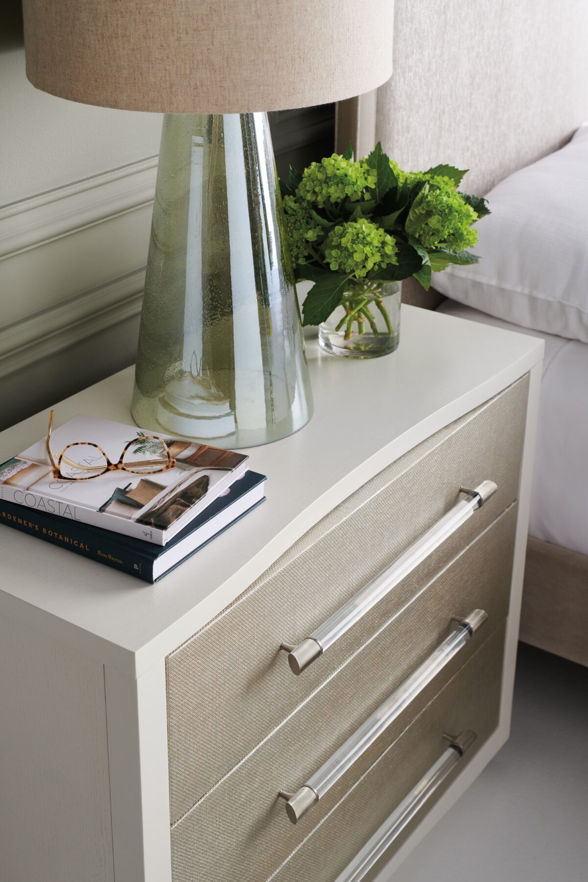 A Clear Touch chest by Caracole — a 38″‑wide three‑drawer chest in Pearly White textured finish, with sun‑kissed silver raffia-wrapped drawer fronts, clear acrylic rod pulls capped in satin nickel, undermount soft‑close guides, and painted pearly-white drawer interiors.