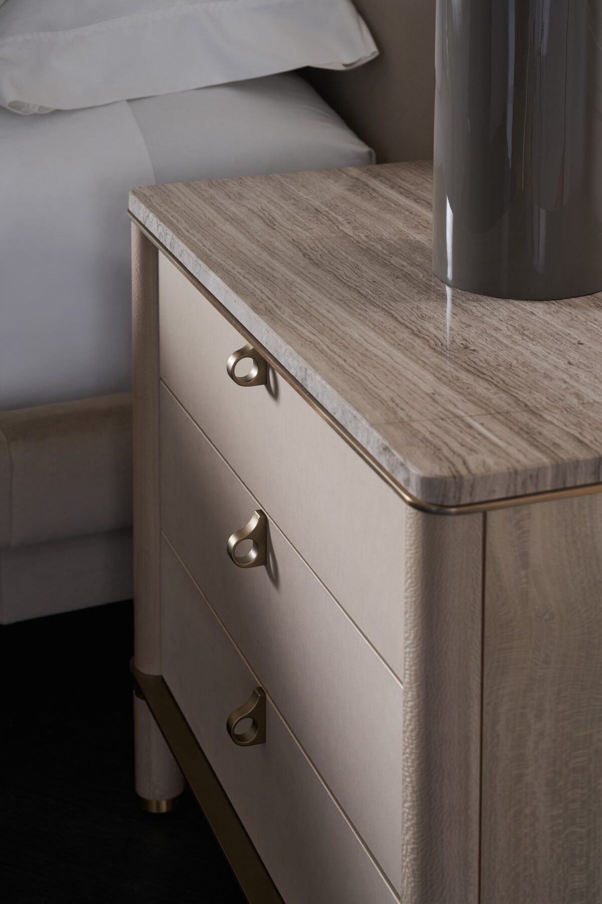 Balance Drawer Nightstand by Caracole — a 28″‑wide modern nightstand in Cremini-finished hardwood with three soft‑touch vinyl-wrapped drawers, topped in polished Silver Travertine stone and supported on round Cremini legs with Lucent Bronze-metal accents and trim.
