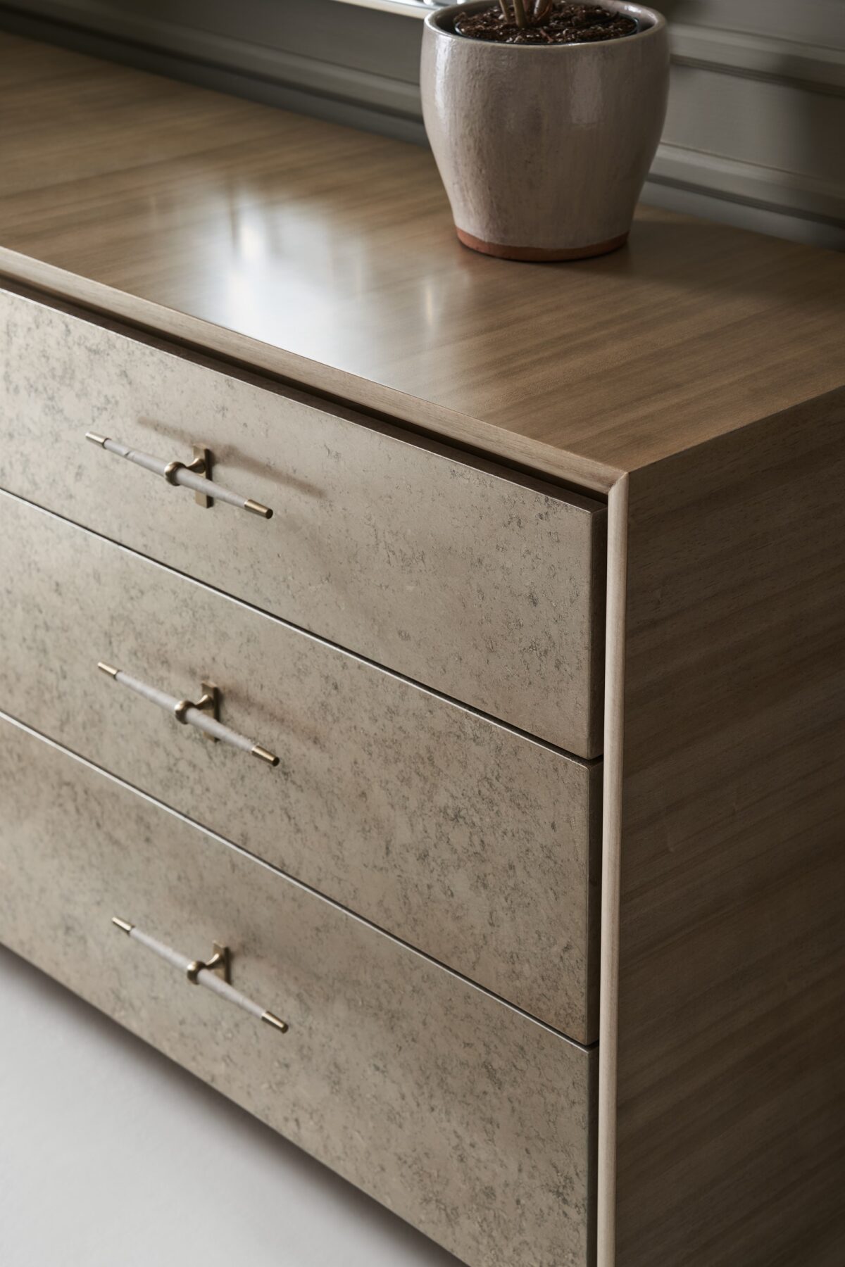 Hang Up Dresser by Caracole — a 70‑inch wide classic dresser with six drawers featuring metallic leaf-finish fronts that shimmer like frosted glass, set in a Dry Martini-finished hardwood frame with recessed metal trim, tapered faux‑leather-wrapped pulls in brushed gold and nickel, soft‑close drawers, and linen-painted interior with top drawer dividers and a removable jewelry tray.