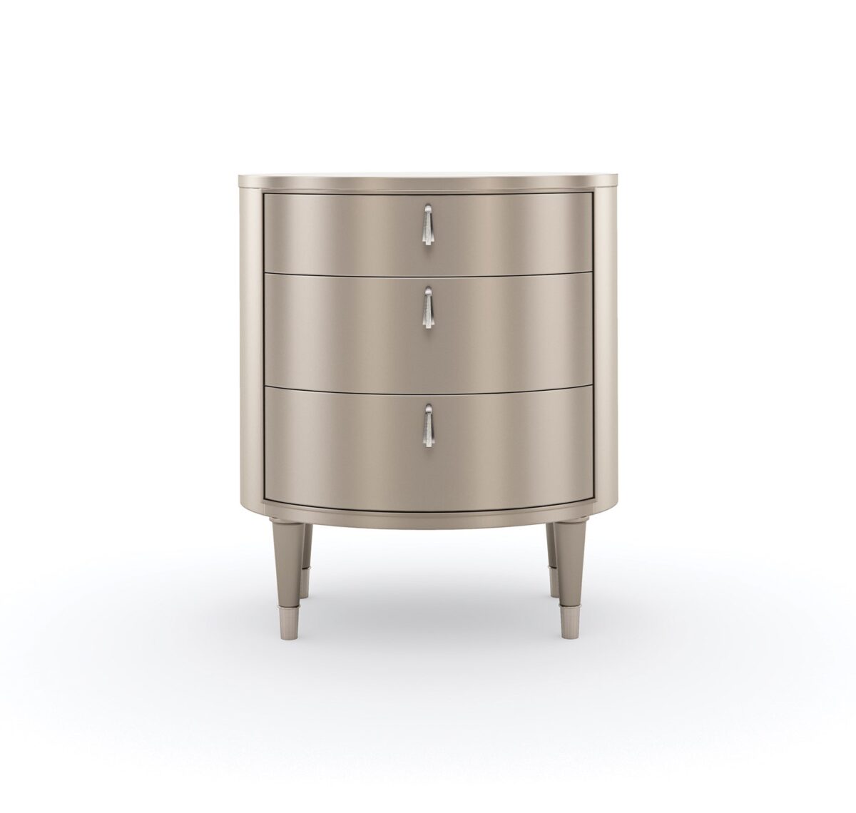 Bedside Beauty Nightstand by Caracole — a 24″-wide oval nightstand with three soft‑close drawers, finished in shimmering soft‑silver paint on Asian hardwood, topped with a softly curved top, accented by polished stainless‑steel ferrules on tapered legs, and elongated Art‑Deco pendant-style drawer pulls with faux-stone centers.