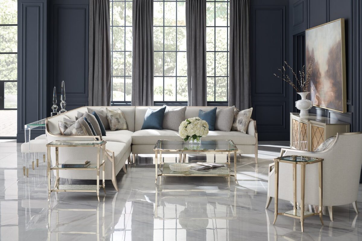 The Caracole X Factor Sofa, a modern classic upholstered in a herringbone performance fabric, featuring a wood-trimmed silhouette with a carved crisscross pattern, gently sloping arms, splayed legs in a metallic Charcoal Leaf finish, and feather-down toss pillows.