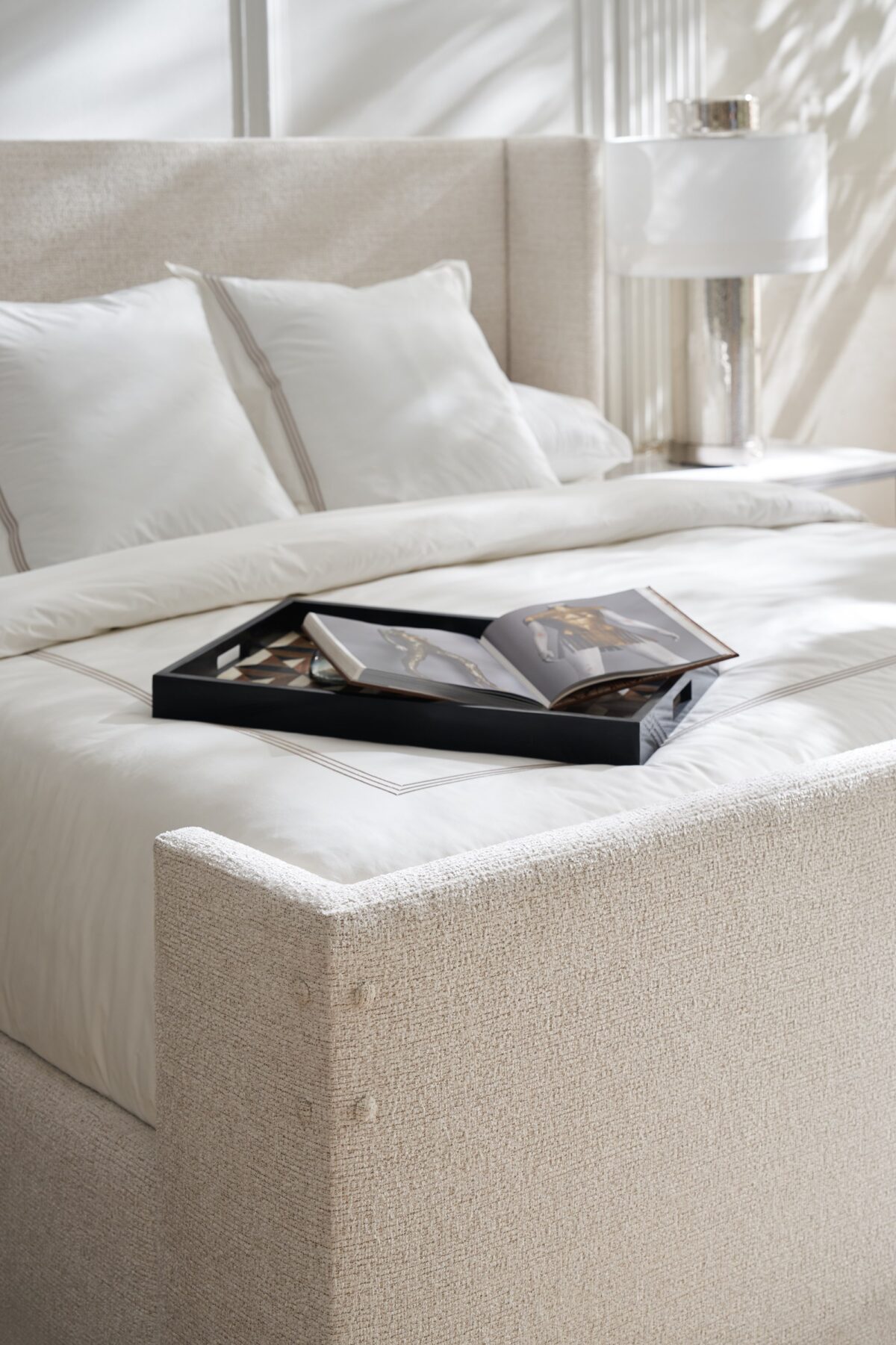 Caracole Shelter Me King Bed featuring a soft chenille upholstered headboard, footboard, and side rails, complemented by decorative buttons and a plinth base in Almost Black finish.