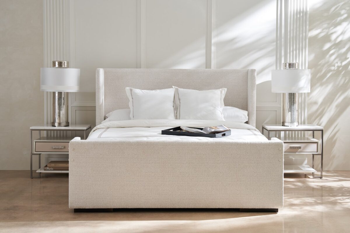 Caracole Shelter Me King Bed featuring a soft chenille upholstered headboard, footboard, and side rails, complemented by decorative buttons and a plinth base in Almost Black finish.