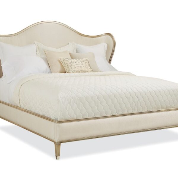 Caracole Bedtime Beauty King Bed featuring a camel-back headboard with curving wings, fully upholstered in cream strie fabric, and an exposed wood rail finished in Auric silver leaf.