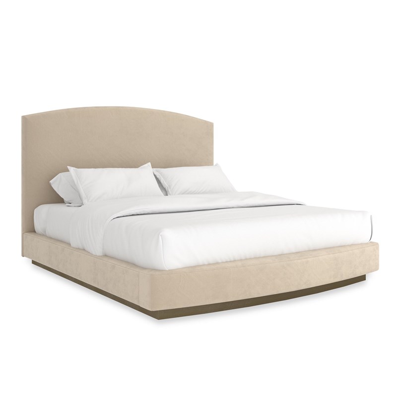 "Caracole Artois King Bed featuring an arched headboard, fully upholstered in pumice-colored performance faux suede, with a wood plinth base finished in Brushed Gold paint."