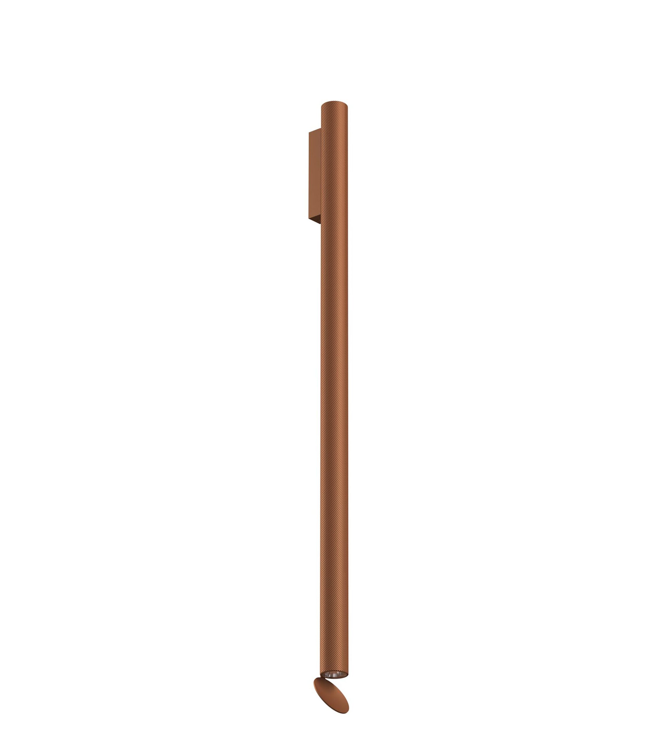 A tall, cylindrical Flos Flauta H1000 Spiga wall lamp in [specify color, e.g., "anodized black" or "anodized copper"], featuring a refined angular etched pattern and dual LED light emission (up and down).
