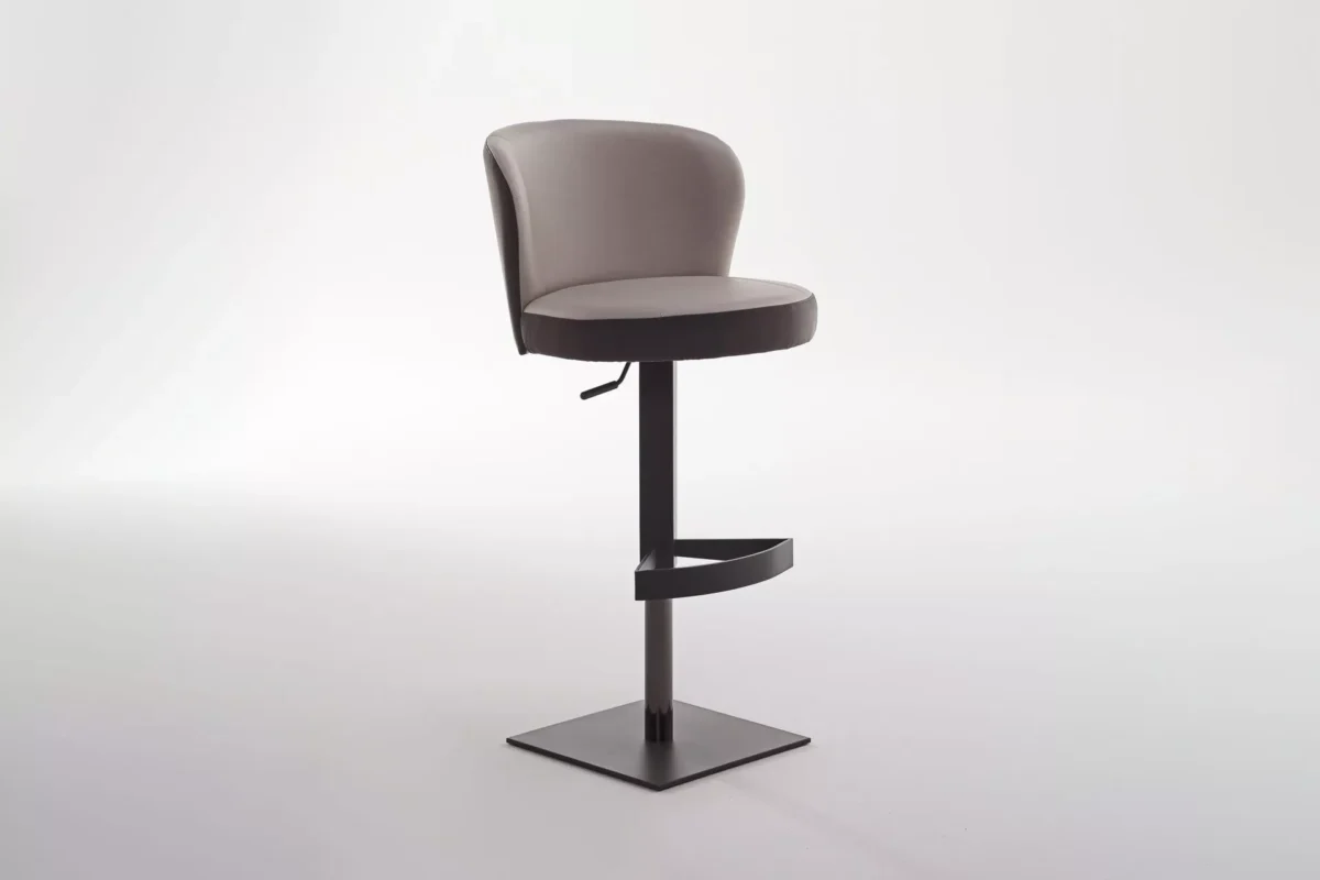 Ocean bar stool by Peressini upholstered in warm grey fabric with a curved low back and brushed stainless steel pedestal base, staged at a white quartz kitchen island.