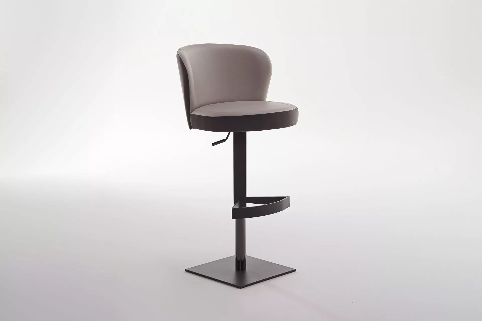 Ocean bar stool by Peressini upholstered in warm grey fabric with a curved low back and brushed stainless steel pedestal base, staged at a white quartz kitchen island.
