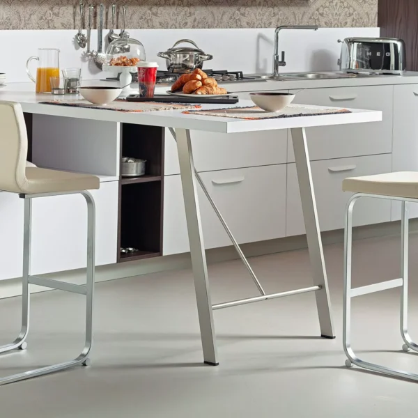 Ocean bar stool by Peressini upholstered in warm grey fabric with a curved low back and brushed stainless steel pedestal base, staged at a white quartz kitchen island.