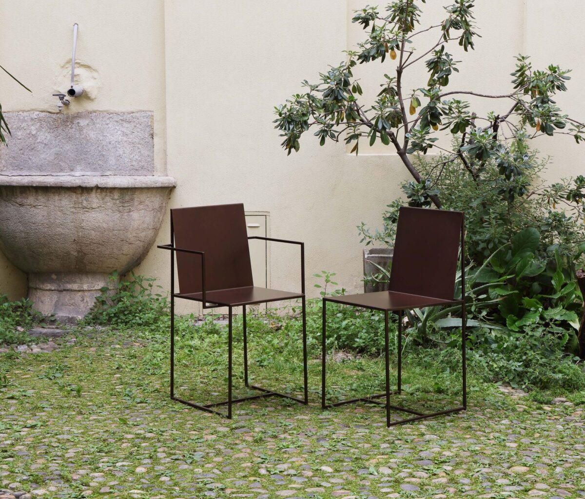 “Slim Sissi Armchair in embossed white metal frame with black leatherette cushion, set in a minimalist office setting.”