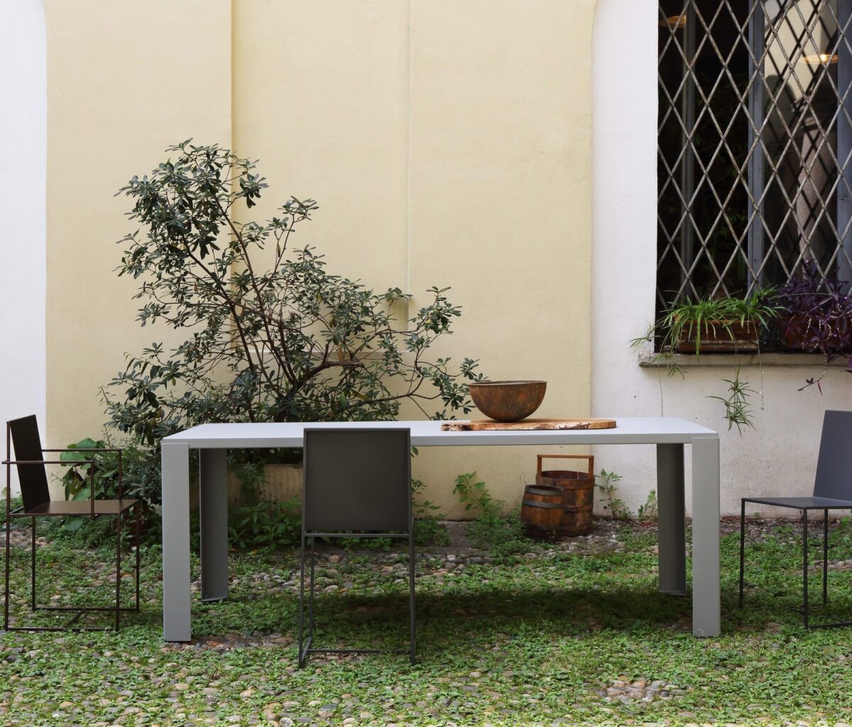 “Outdoor arrangement of Slim Sissi Armchair chairs around a patio table in gun-metal finish, blending indoor elegance with garden charm.”
