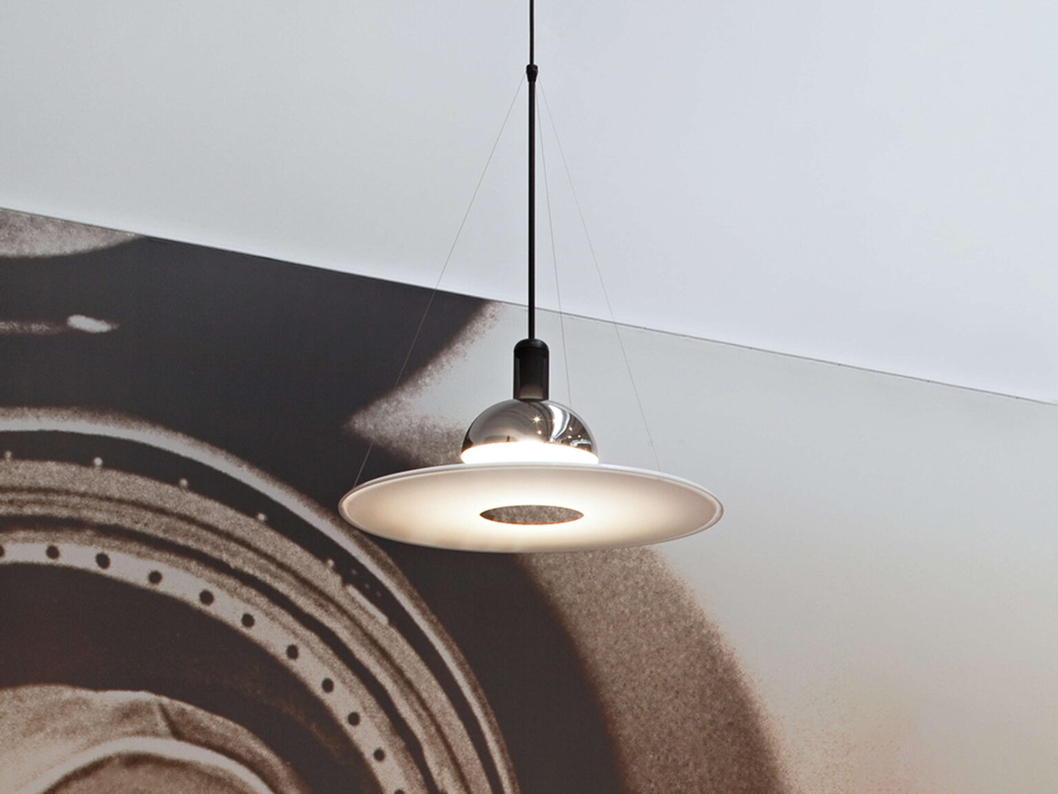 Side view of the Frisbi pendant showing its flying saucer–shaped white diffuser plate, polished nickel reflector, and black stem.