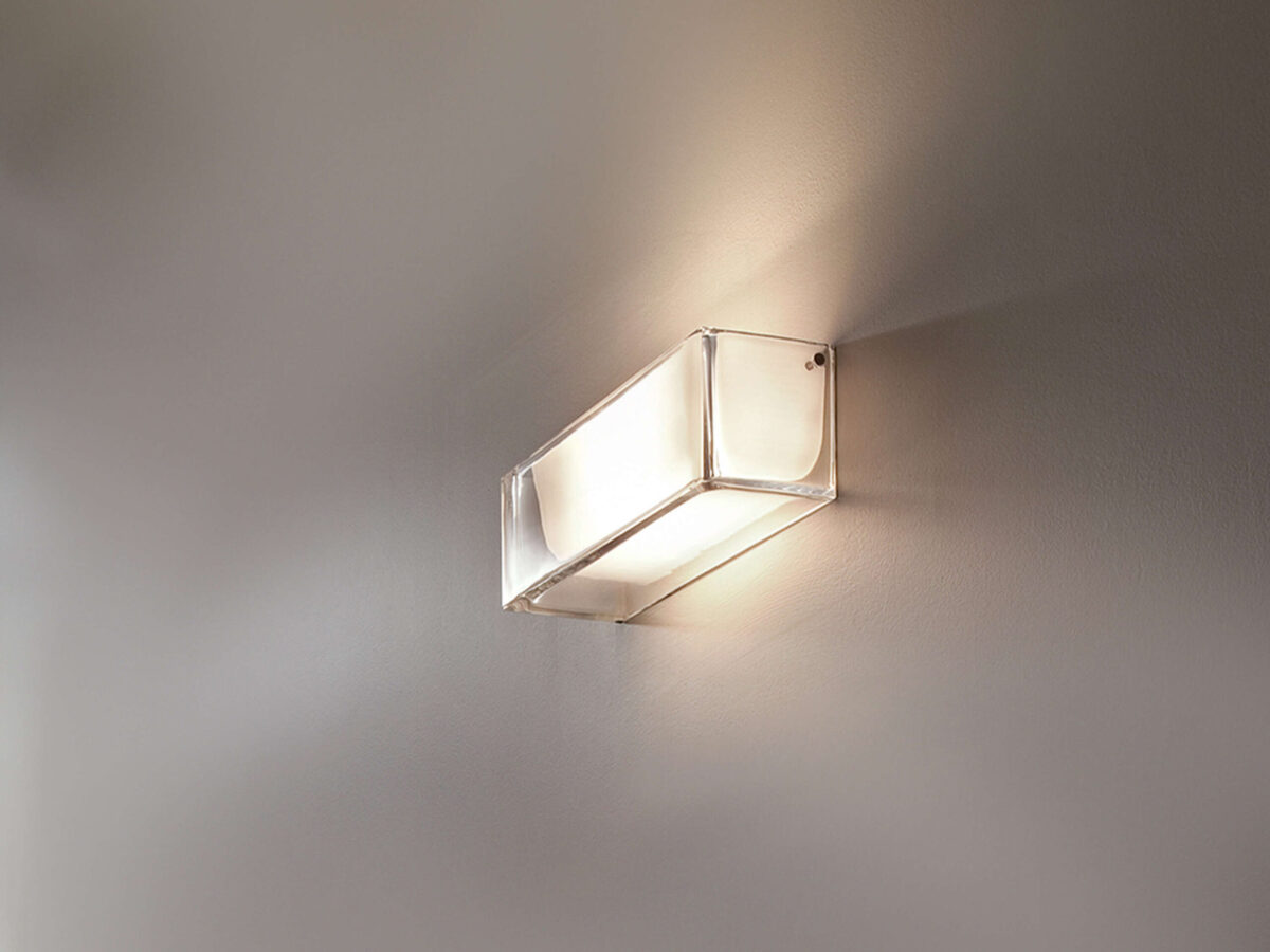 The Flos Ontherocks HL, a minimalist wall light designed by Antonio Citterio, characterized by its solid transparent glass exterior and inner diffusing element, creating a soft yet powerful glow.