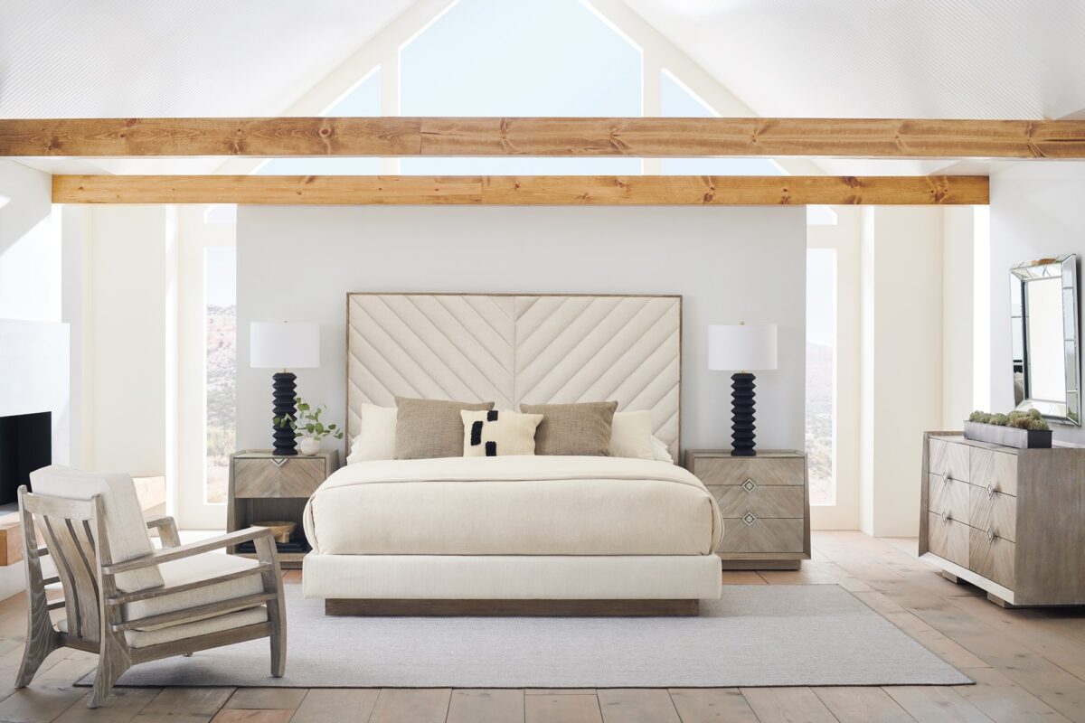 Caracole Meet U in the Middle King Bed with a fully upholstered frame, chevron-patterned headboard, and exposed Black Stain Ash wood trim, resting on a plinth base.