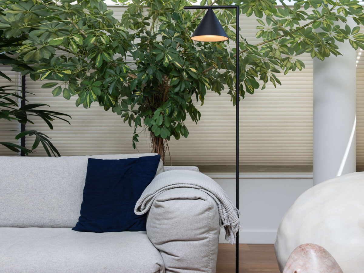 Brushed brass stem and cone lamp with white Carrara marble base, casting warm 2700 K light over a living area.