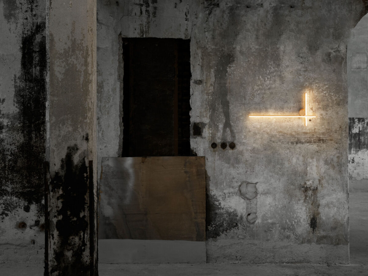 A contemporary wall-mounted Flos Coordinates Wall 2 fixture, showcasing its clean lines and precise angles, with a vertical bar intersecting a horizontal one, each emitting a soft, warm LED glow.