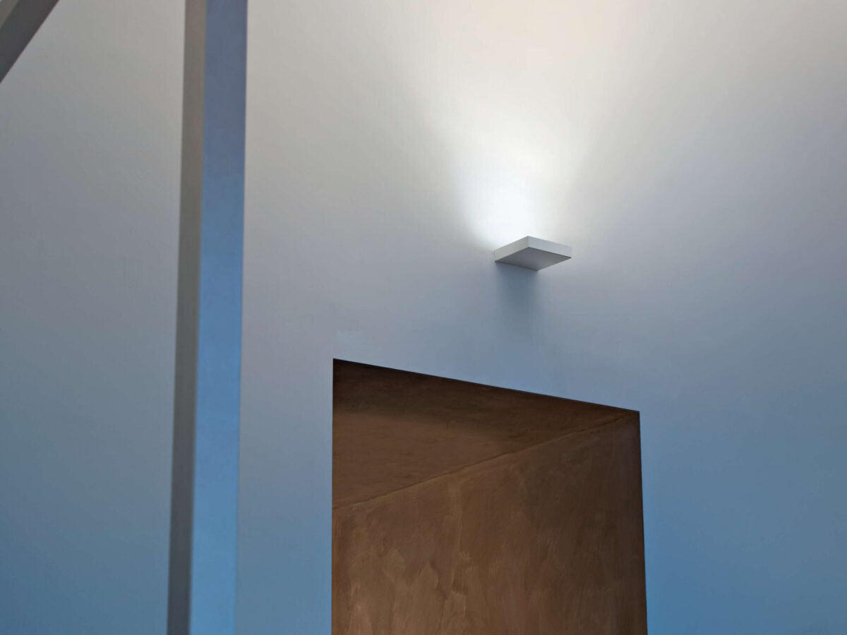 The minimalist Flos Fort Knox Wall LED Mini by Philippe Starck, a compact (150x150mm) wall light that conceals its light source while casting a powerful wash of light onto the ceiling or upper wall.