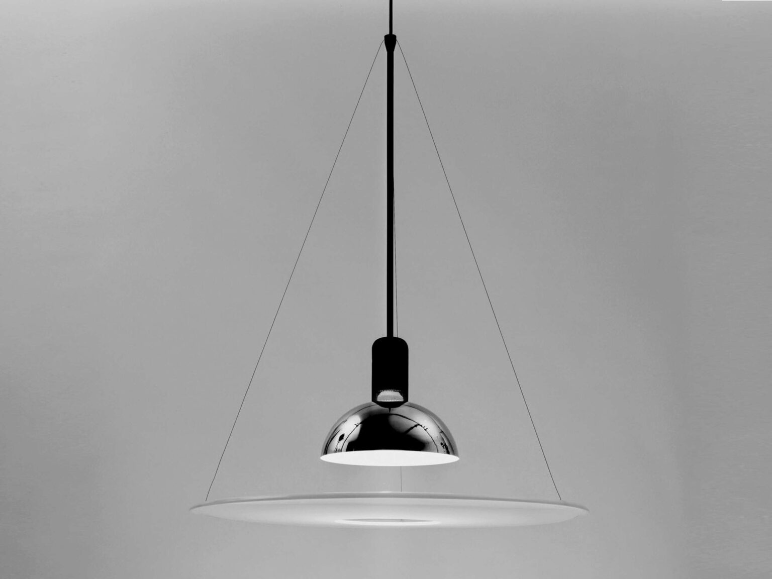 Frisbi lamp in matte black finish, suspended over a dining table, casting both direct downward and soft reflective light.