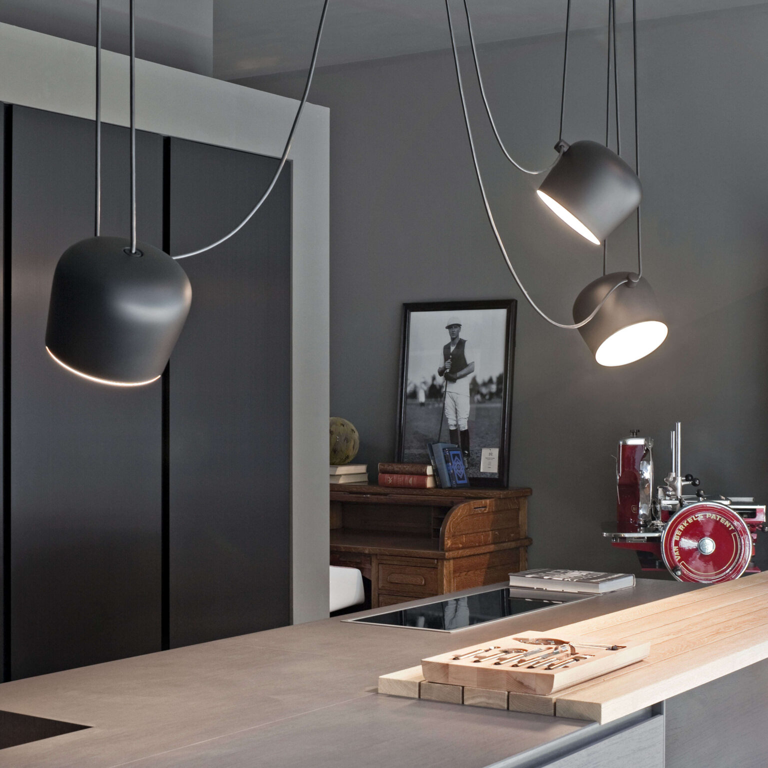 Side view of a trio of Aim pendants in black, each head tilted differently and draped cables creating sculptural lines above a dining table.