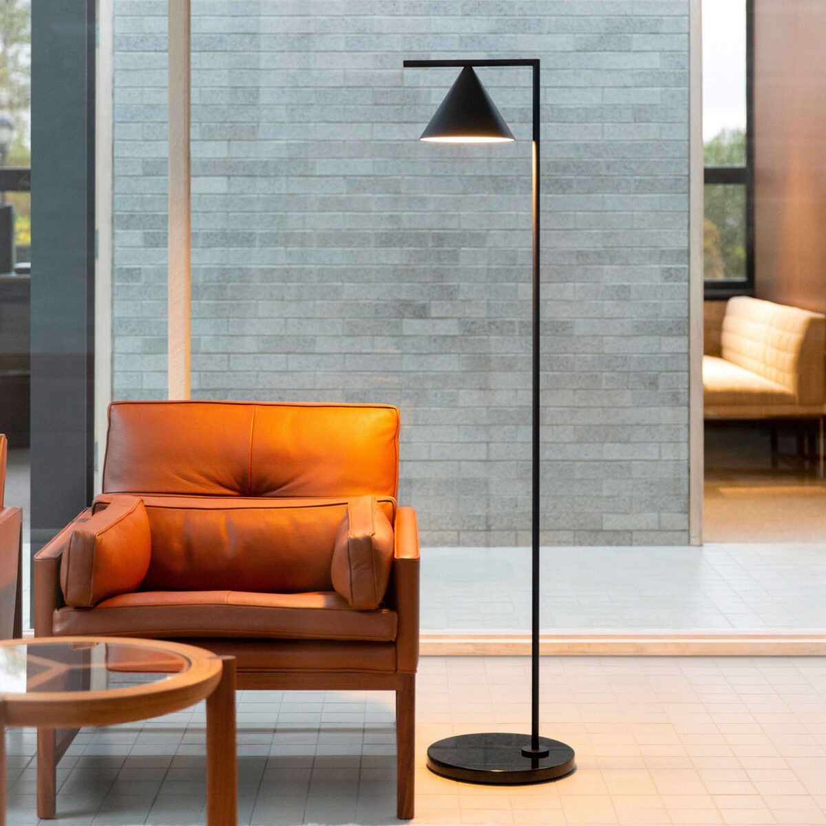 Modernist floor luminaire: polished cone shade, black cable with foot dimmer, and solid stone base.