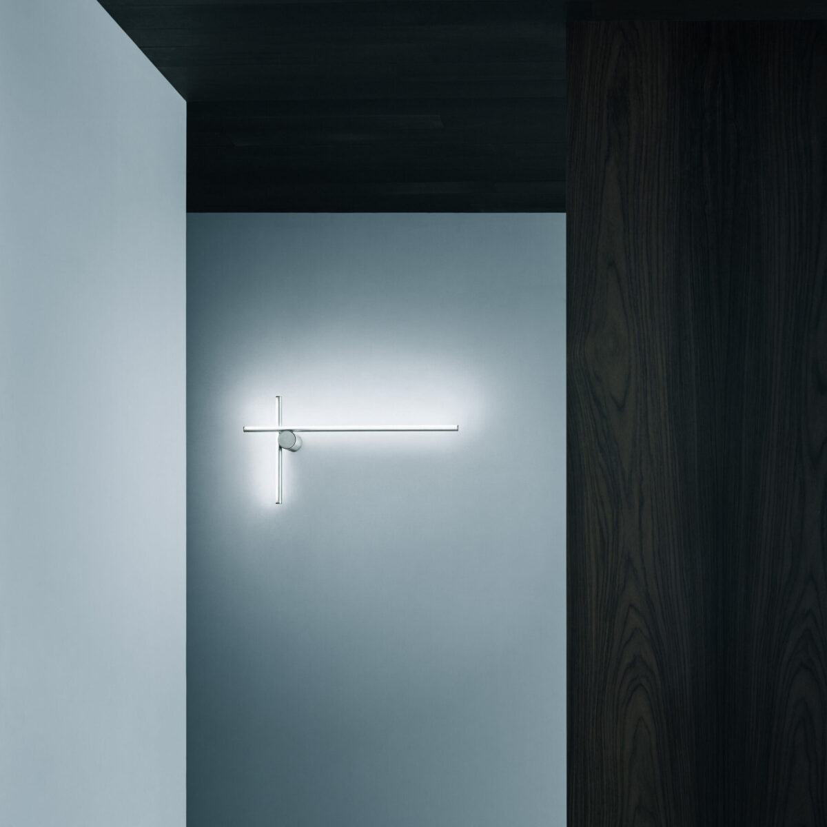 The Flos Coordinates Wall 2 by Michael Anastassiades, an architectural wall lamp featuring two slender, perpendicular illuminated rods made of anodized aluminum and opal silicone, designed to provide ambient light.