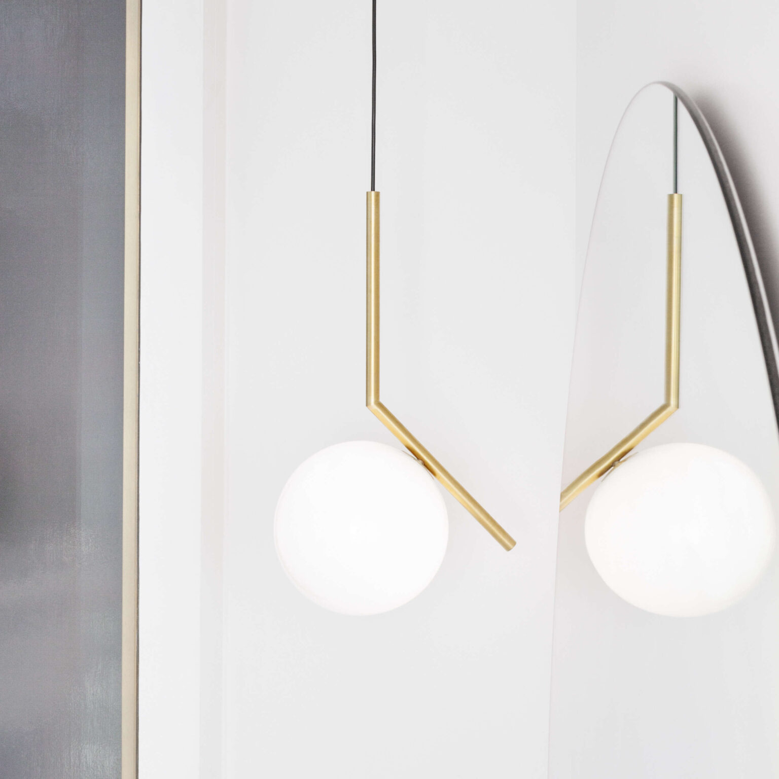 Pair of brushed brass IC Lights pendants with spherical diffusers, suspended asymmetrically in a modern living room.