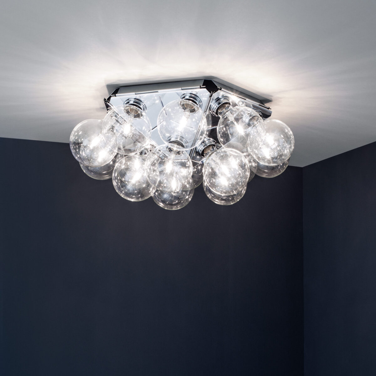 The iconic Flos Taraxacum 88 C/W by Achille Castiglioni, a large, multi-bulb fixture with a polished aluminum frame from which numerous clear spherical bulbs extend, offering direct and reflected light.