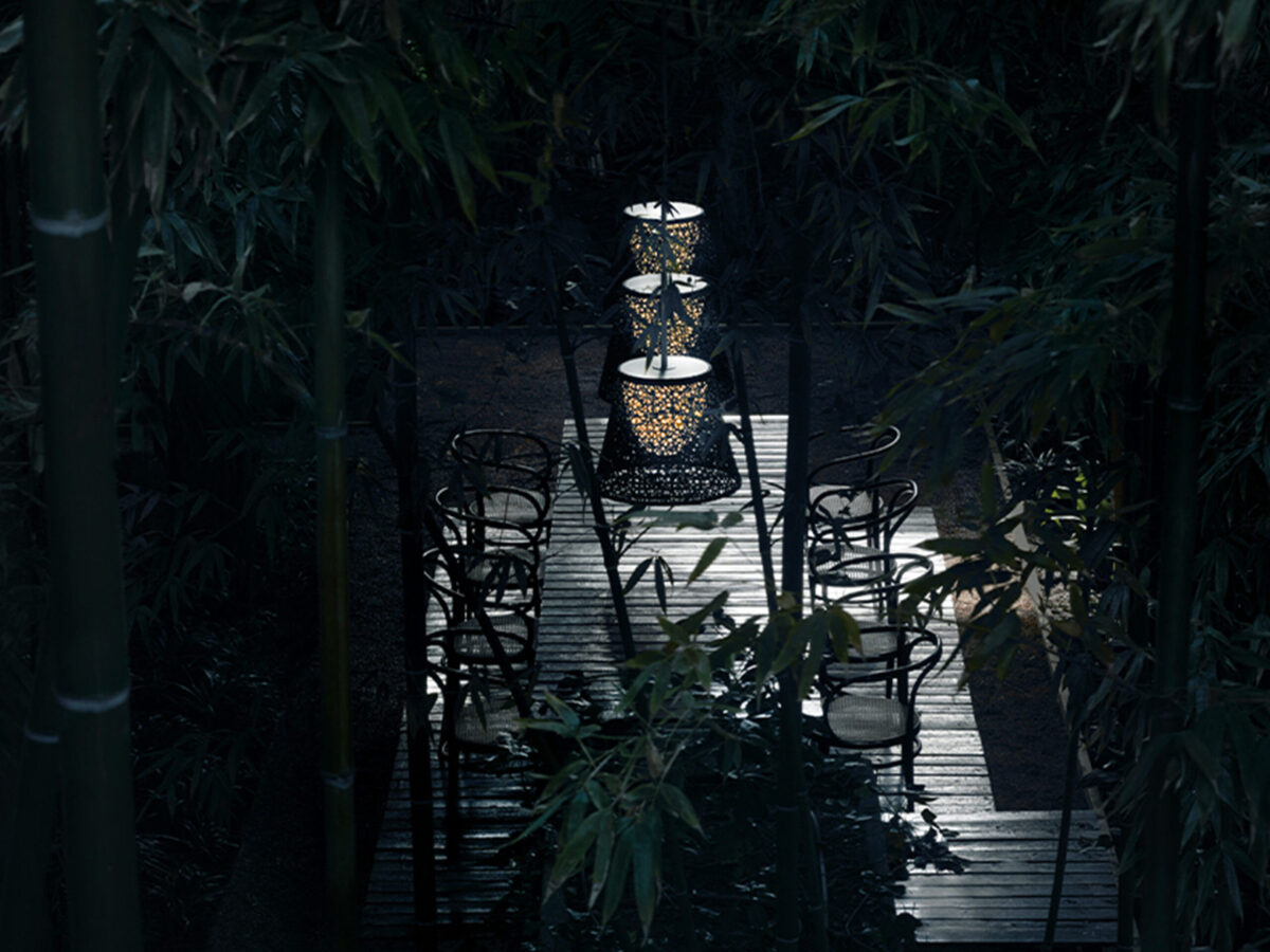 Pendant lamp with a fluted PVC shade in neutral green tone, Romeo Outdoor C3 by Flos mounted against a lush green wall.