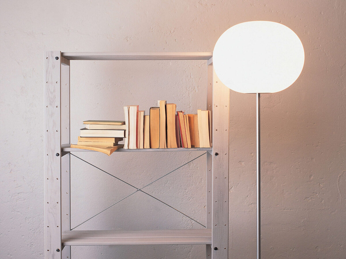 Silver-finished stem floor lamp casting soft, diffused light from its white glass globe in a minimalist room.
